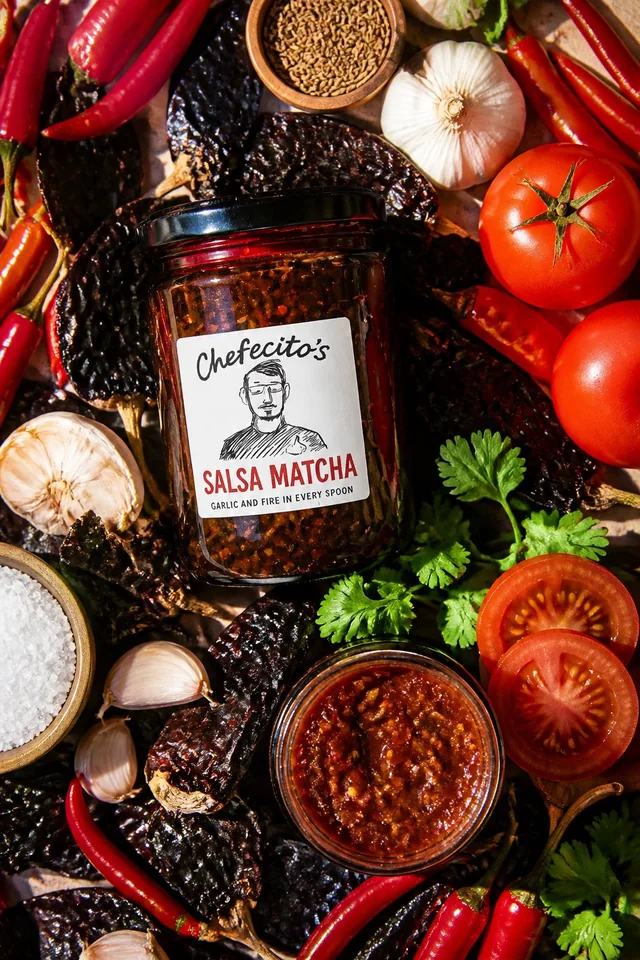 Chefecito’s Salsa Macha test-batch jar surrounded by dried chiles, garlic, tomatoes, and herbs